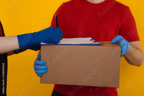 Delivery man in the red T-shurt and gloves holding an empty cardboard box isolated on yellow background. Woman accepting an order