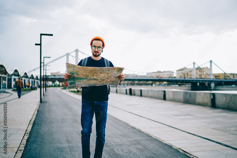 Pensive casually dressed hipster guy walking on urban setting in town with map searching route for destination, young caucasian male traveler strolling in city searching showplaces during tour. Pensive casually dressed hipster guy walking on urban setting in town with map searching route for destination, young caucasian male traveler strolling in city searching showplaces during tour.