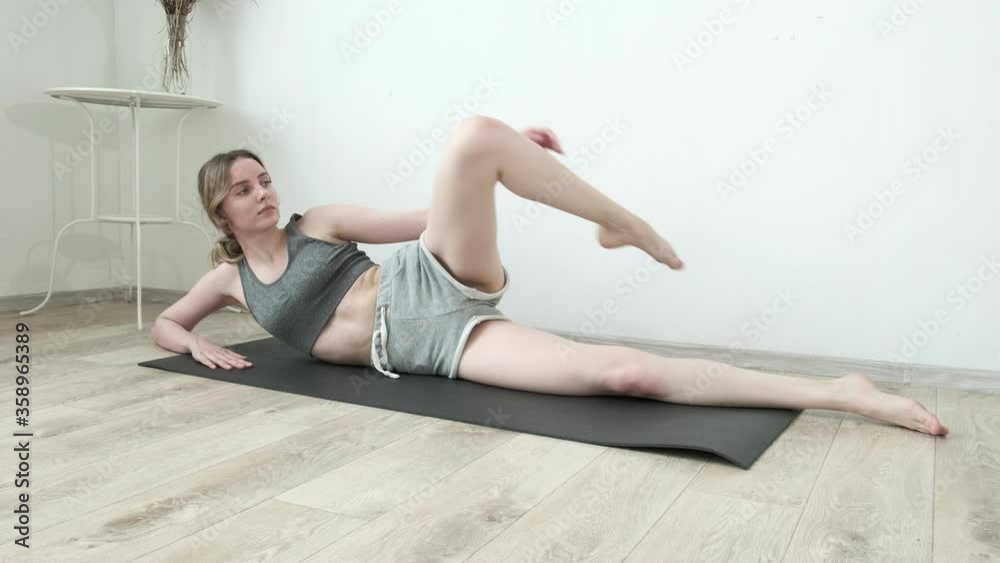 young slim pretty girl in sportswear practicing yoga at home. fit flexible female in shorts raises leg up lying on mat. fitness training, sport, yoga, healthy lifestyle, stretching, pilates, workout young slim pretty girl in sportswear practicing yoga at home. fit flexible female in shorts raises leg up lying on mat. fitness training, sport, yoga, healthy lifestyle, stretching, pilates, workout