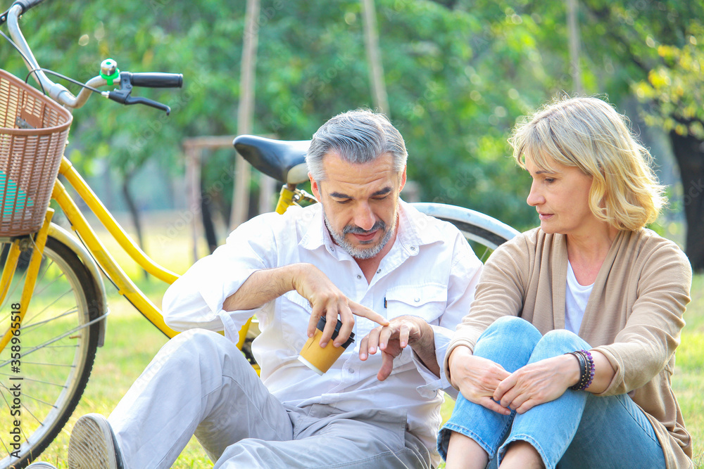 Obraz premium Senior couple sit on the lawn in the park happily and the bike is parked in the back. The concept of living after retirement