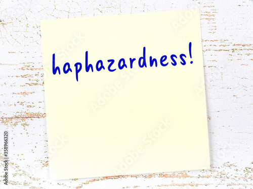 Yellow sticky note on wooden wall with handwritten word haphazardness photo