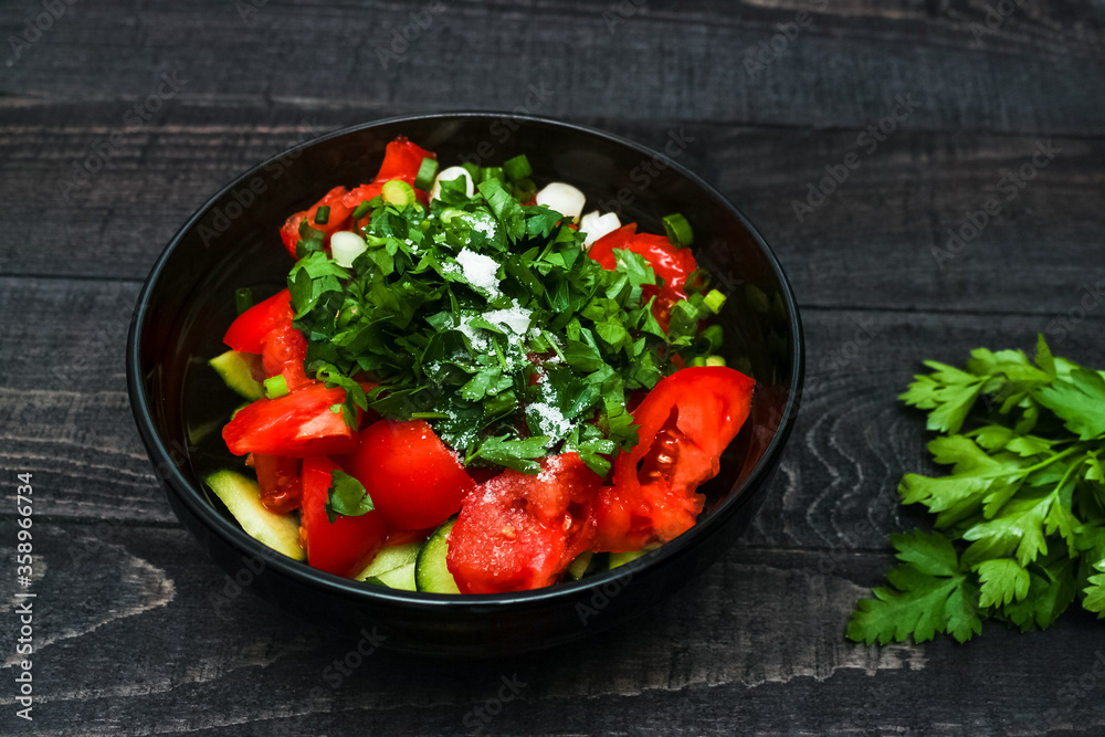 Fresh vegetables salad from tomatoes and cucumbers in black bowl on black wooden background. Healthy food concept. Fresh vegetables salad from tomatoes and cucumbers in black bowl on black wooden background. Healthy food concept.