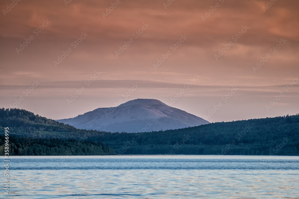 Lake, coniferous forest and mountain in the sunset light
