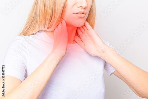 Female checking thyroid gland by herself. Close up of woman in white t- shirt touching neck with red spot. Thyroid disorder includes goiter, hyperthyroid, hypothyroid, tumor or cancer. Health care
