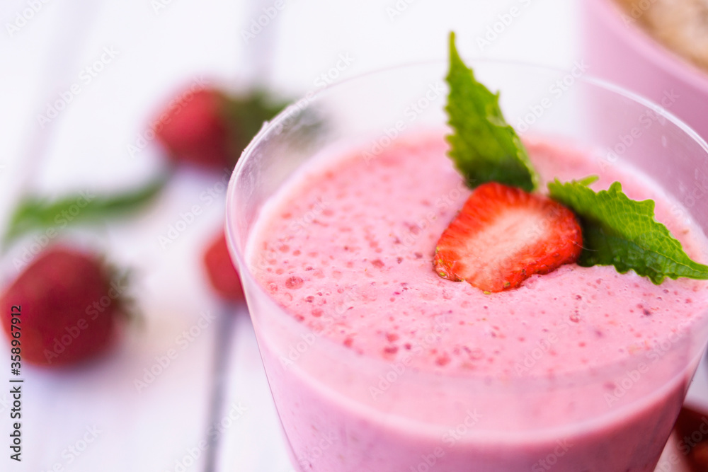 Cocktail with strawberries and milk in a glass decorated with mint and strawberries. Nearby is a pink cup with Hercules flakes, and loose strawberries on a white wooden background. Cocktail with strawberries and milk in a glass decorated with mint and strawberries. Nearby is a pink cup with Hercules flakes, and loose strawberries on a white wooden background.