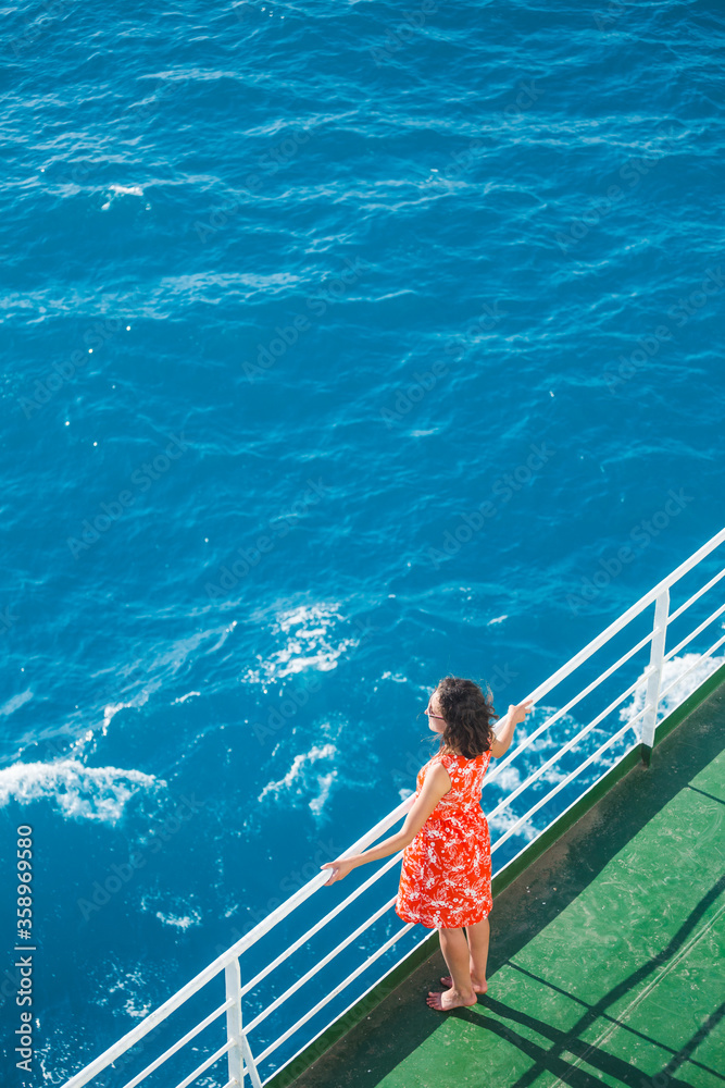 A girl is standing near the fence on a ship and looking at the sea, view from above A girl is standing near the fence on a ship and looking at the sea, view from above