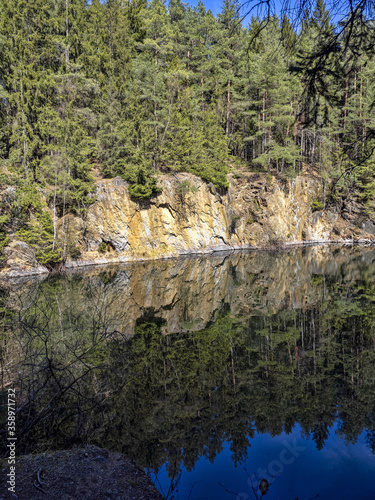 Trees and rocks are reflected in the calm water surface
