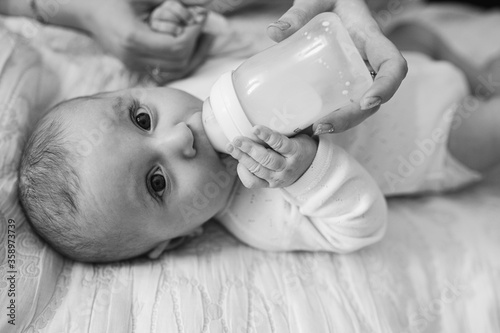 A little girl drinks milk from a bottle. Black and white photo