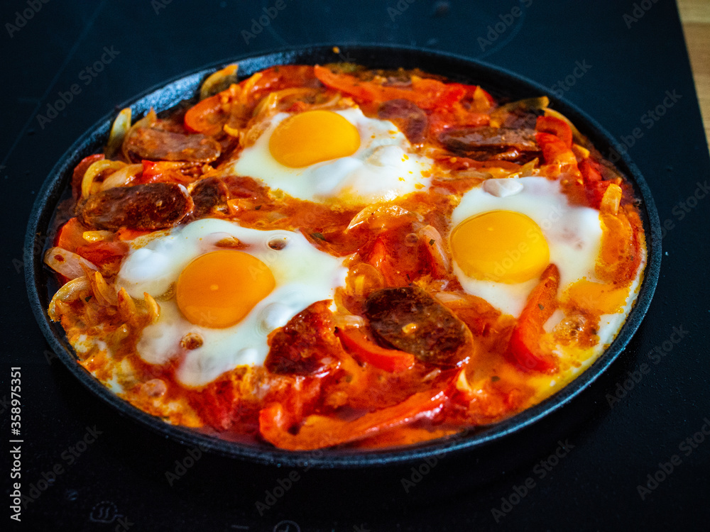 Shakshuka - fried eggs with chorizo and vegetables in frying pan
