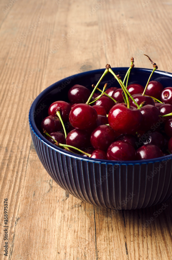 Vertical image.Bowl full of ripe dark red cherries on the wooden table