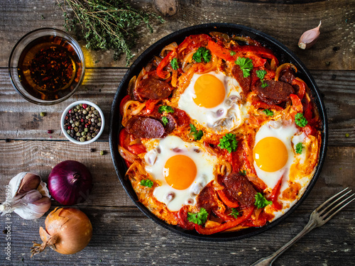 Shakshuka - fried eggs with chorizo and vegetables in frying pan 