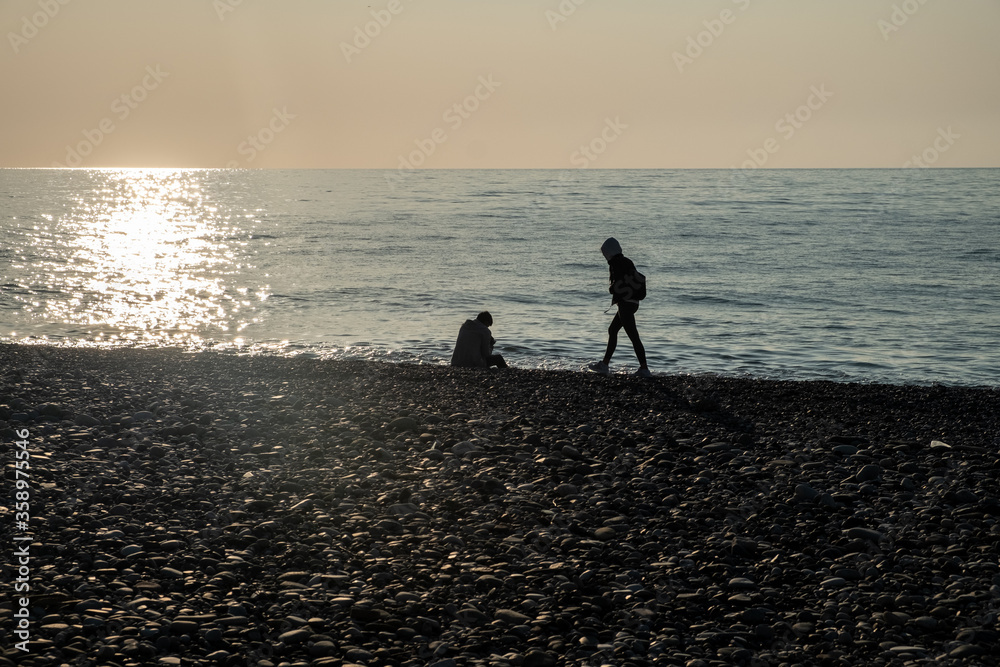 Silhouettes of people on the background of the sea and sunset. Solar path on the water. Small ripples ha surface of the water. Beach, a beach from a galois. Evening. Spring. Georgia.