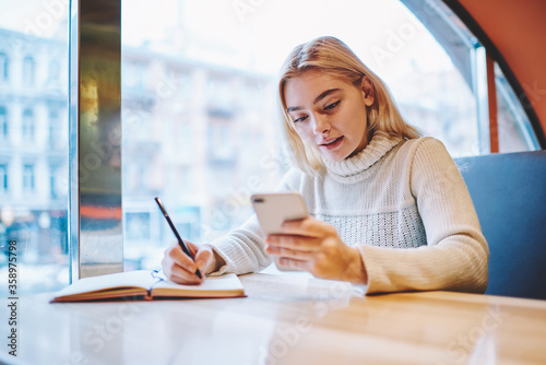 Free Download Teen girl reading new message on smartphone while learning in cafe interior prepare homework task,young female hipster checking notification on cellular creating article for blog publication - GFXLoad