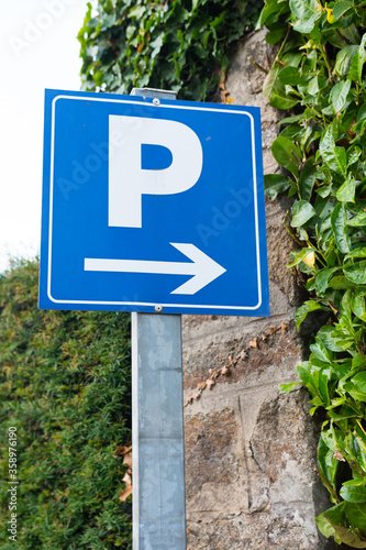 Blue parking sign (Europe, France). Capital letter P with an arrow to the right. Big close up with a blurred background. Green foliage. Vertical shot.