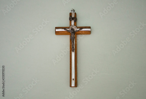 Small wooden / matal cross hanging on light pastel background in old vintage house