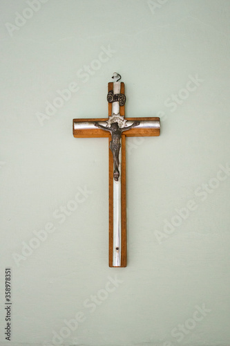 Small wooden  / matal cross hanging on light pastel background in old vintage house