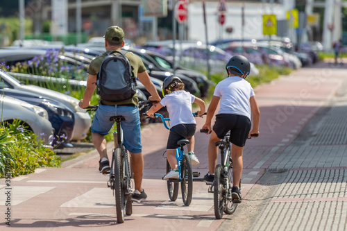rear view of a man with children riding bikes on a bicycle path in the city, sunny day