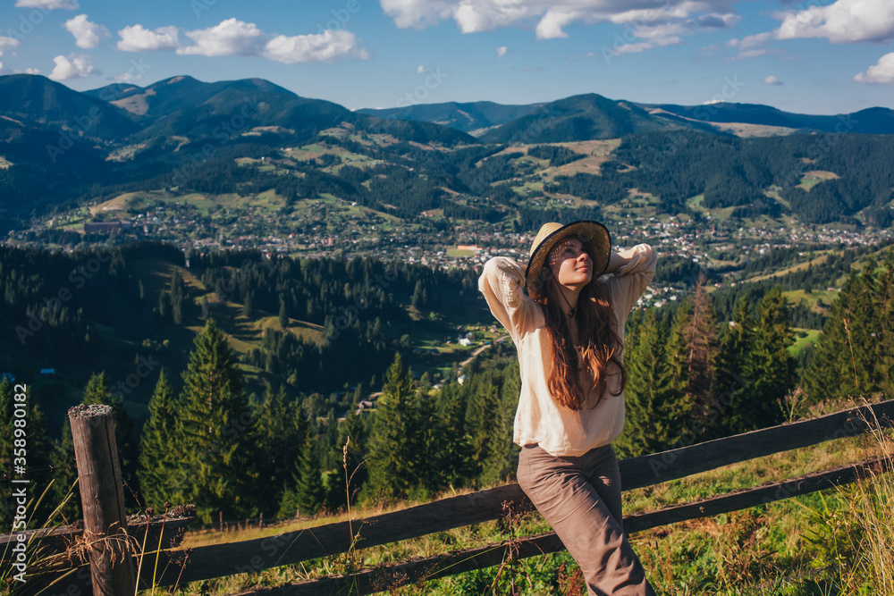 a girl in a hat with long hair resting in the mountains. She has a view of the mountains behind her. view of the Carpathians