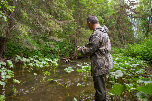 fisherman with a spinning rod stands on the shore of a small northern river