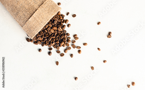 A burlap bag with coffee beans on a white, scuffed background. Concept of a popular invigorating drink. selective focus.