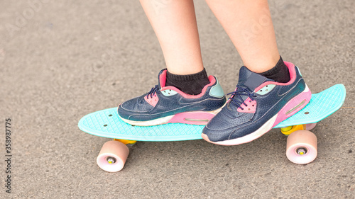 Close up view of girls feet in colorful sneakers riding on turquoise penny skate board on asphalt. Summer sports activities for teens, active kids lifestyle.