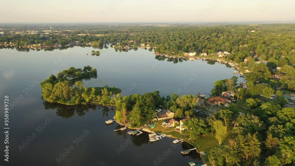 Aerial view of american suburb at summertime.  Establishing shot of american neighborhood. Real estate, residential houses with boat launch on the lake shore. Drone shot, from above, sunrise, morning