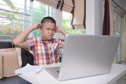 An Asian male student is stressed. Online learning with teachers by video chat and looking at the laptop through the internet at home. Due to the coronavirus crisis (Covid-19). Home learning concepts.