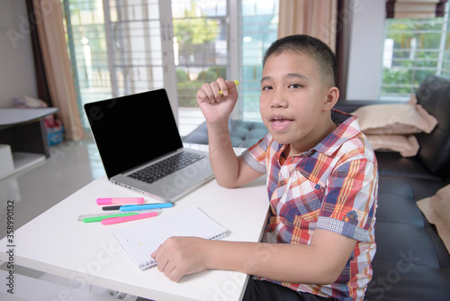 An Asian male student feel relaxed and smiling. When he have finished his homework on the online study over the internet at home. .Due to the coronavirus crisis (Covid-19). Home learning concepts.