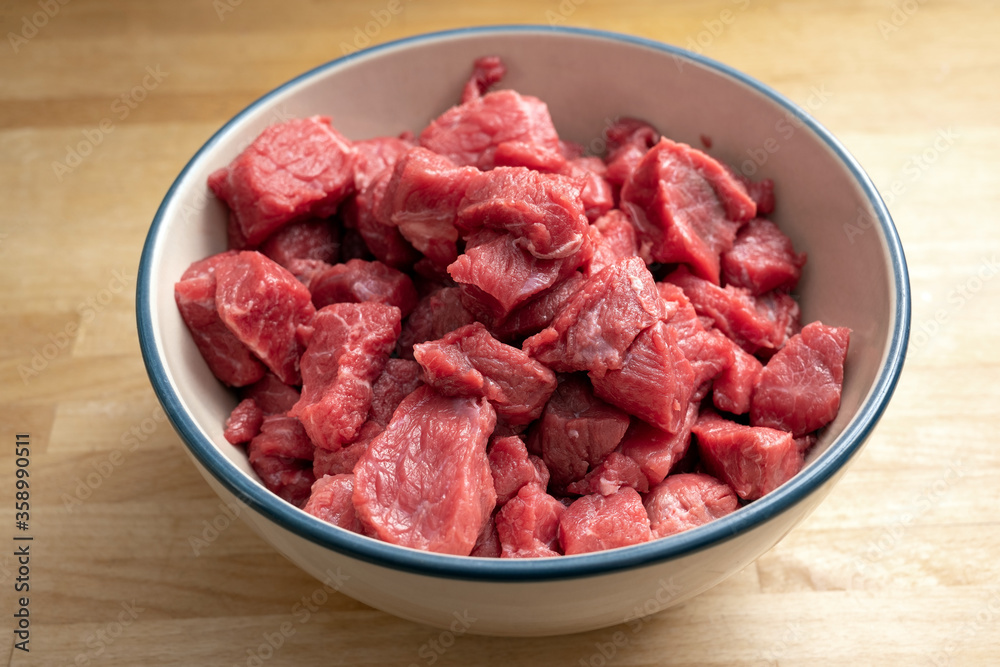 Fresh diced raw beef for goulash or stew in a bowl on a wooden table, cooking at home during coronavirus pandemic, selected focus