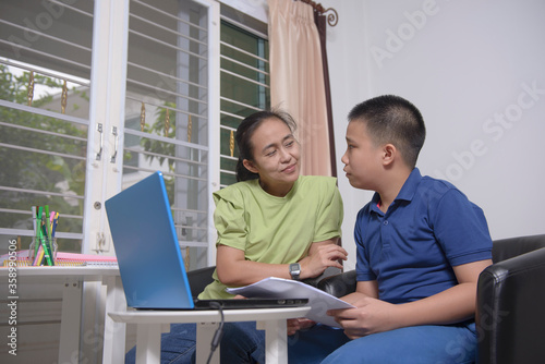 An Asian student does not understand the lessons of online learning at home on a laptop. And his mother is helping to solve problems. Concepts of home-learning and Prevention Coronavirus(COVID-19).