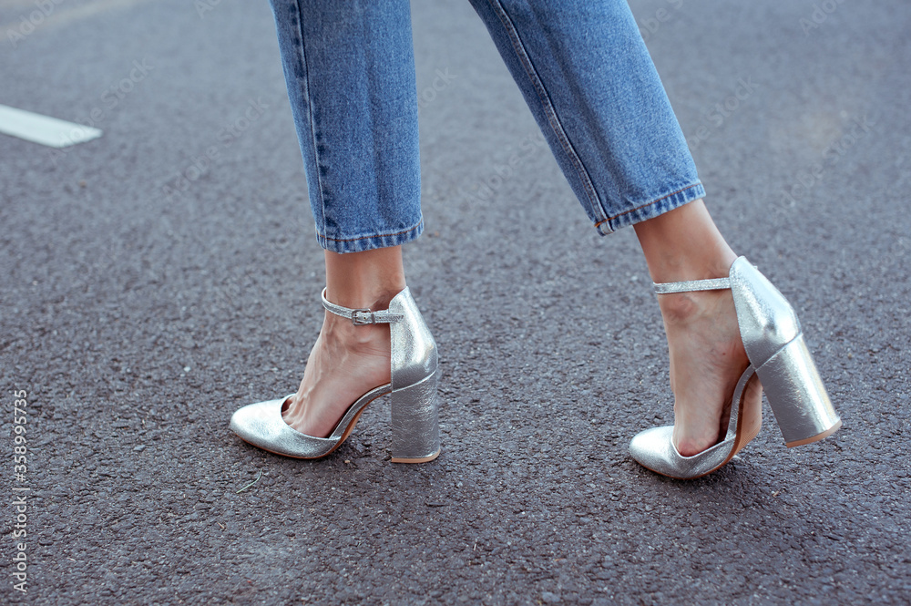 Fashionable young woman wearing blue jeans and silver high heel shoes. Street style.