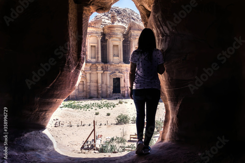 Young girl on her back at the entrance of a cave observing the Petra monastery ad-deir