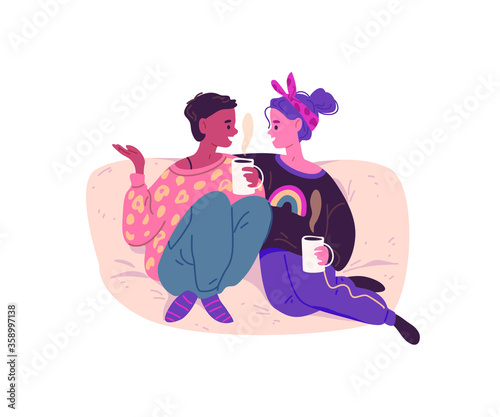 Young women sitting on the couch and talking. Friends drink coffee at home.  Girls stay at home during Coronavirus 