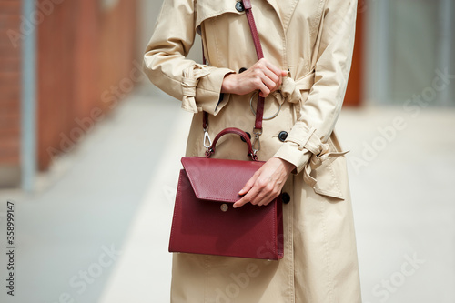 Fashionable young woman in cropped jeans, blue blouse, beige trench and two handbag .She is wearing blue high heel shoes. Street style. © Olha