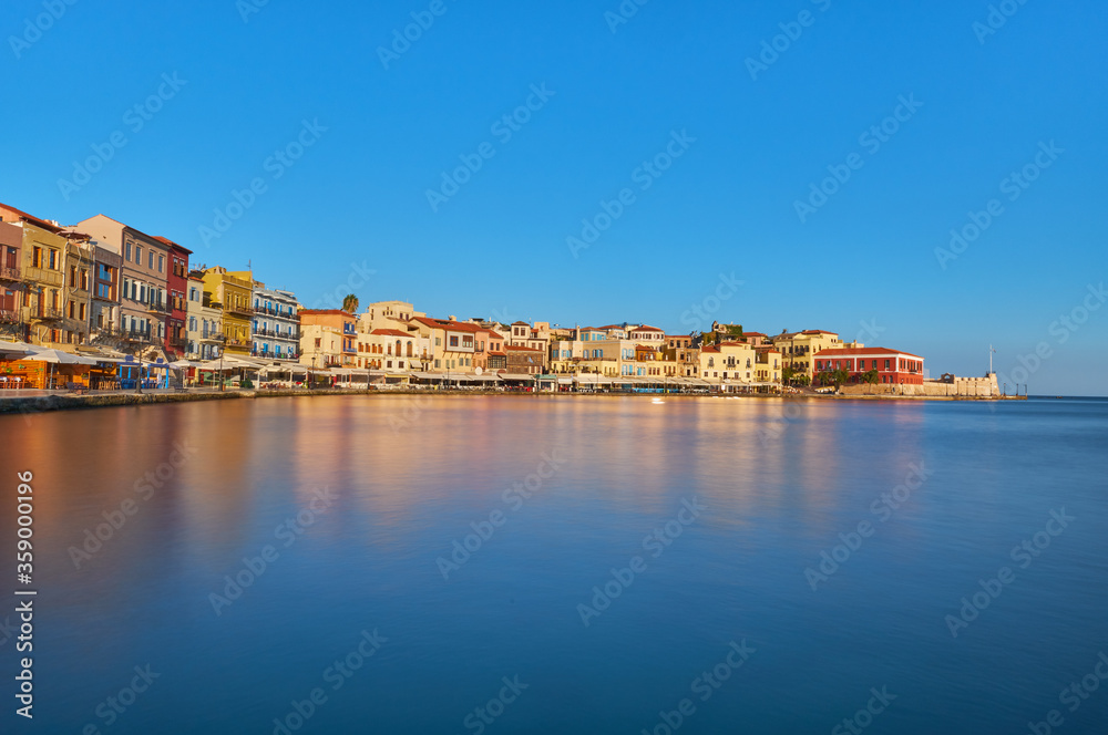 View of old harbor of Xania of Crete island Greece. Taverns on the pier in the rising sun with slow motion effect water in the foreground. Bay of Xania on sunny summer day. 
