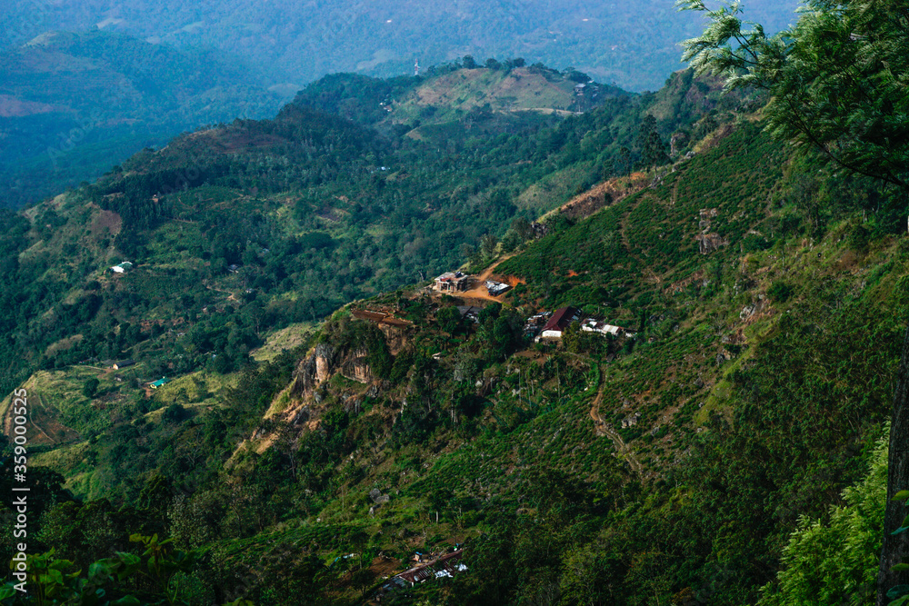 View from above to the green mountains, pathway, smoke and village in Sri Lanka
