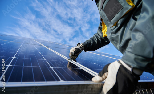 Close up of man technician in work gloves installing stand-alone photovoltaic solar panel system under beautiful blue sky with clouds. Concept of alternative energy and power sustainable resources. photo