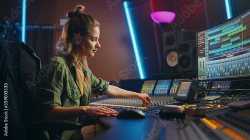 Beautiful, Stylish Female Audio Engineer and Producer Working in Music Recording Studio, Uses Mixing Board and Software to Create Cool Song. Creative Girl Artist Musician Working to Produce New Song