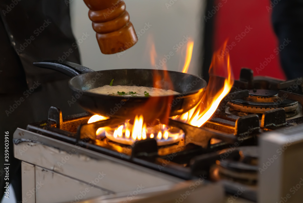 Chef seasoning a pan of food over flames