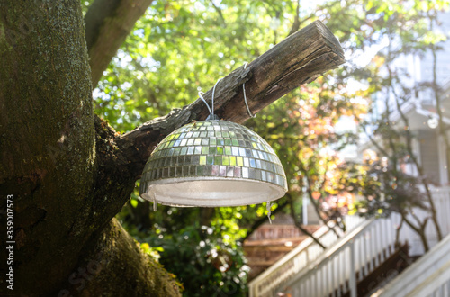 Disco ball on a tree branch, in the backyard. Closeup. Concept for backyard staycation or party. Soft bokeh background with stairs and leaves.