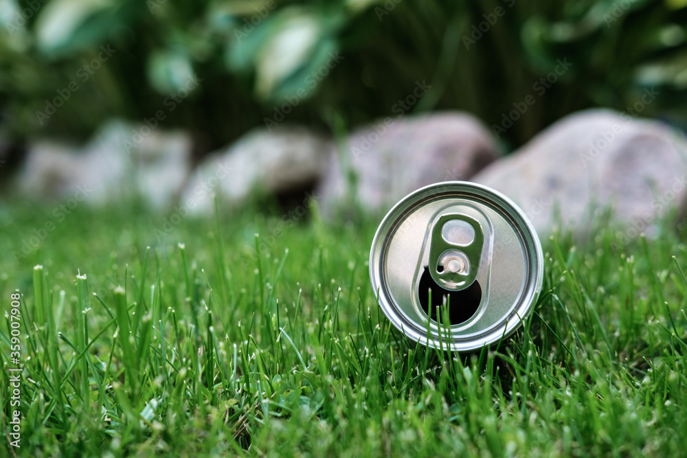 An open aluminum can lies in the grass, amid a mown lawn and a flower bed framed with stones. An open aluminum can lies in the grass, amid a mown lawn and a flower bed framed with stones.