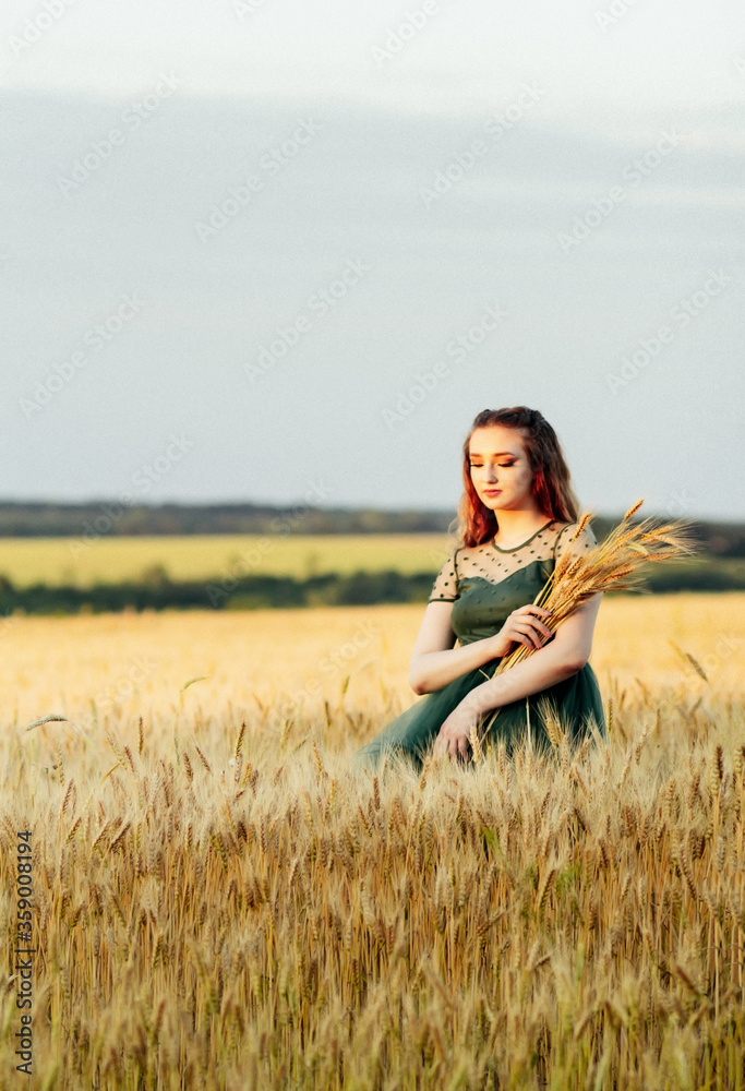 Beautiful woman in green dress on field with sheaf of wheat in hand at sunset light, girl enjoying summer nature landscape, harvest Beautiful woman in green dress on field with sheaf of wheat in hand at sunset light, girl enjoying summer nature landscape, harvest