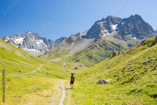 Woman with backpack hiking towards mountain top, scenic glacier and dramatic landscape summer fitness wellbeing selective focus rear view, freedom concept