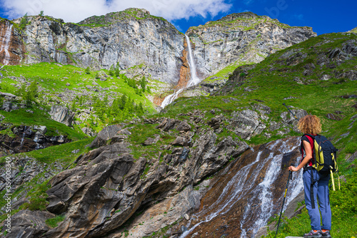 Lady hiker looking at waterfall on mountain. One person with backpack outdoor activity in scenic alpine landscape, summer vacation on the Alps, fitness wellbeing freedom