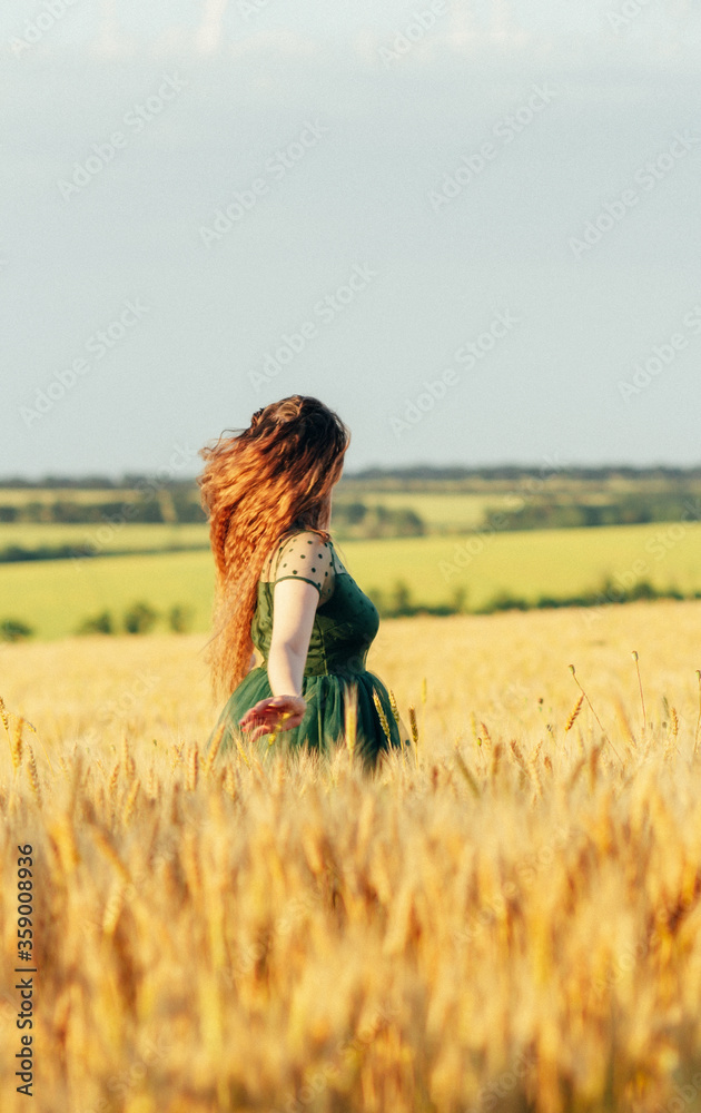 Beautiful woman in green dress with flying long hair, girl walking in field of wheat, girl enjoying summer nature, freedom concept Beautiful woman in green dress with flying long hair, girl walking in field of wheat, girl enjoying summer nature, freedom concept