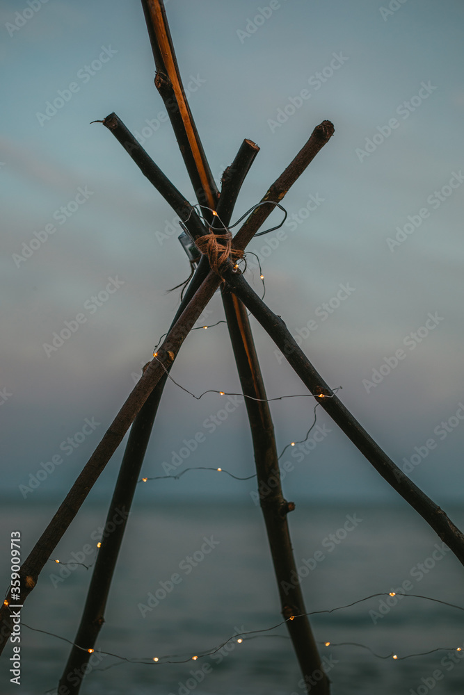 Fototapeta premium Branches teepee with little lanterns on the beach