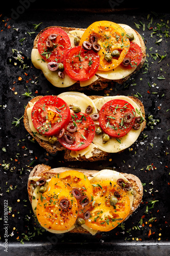 Sandwiches with sourdough bread,  cheese and tomatoes sprinkled herbs on a black background, top view