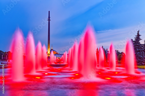 Fountains with red lights in Victory Park Poklonnaya Gora. Night illumination, summer evening in the city. Background - Victory Memorial in World War II.