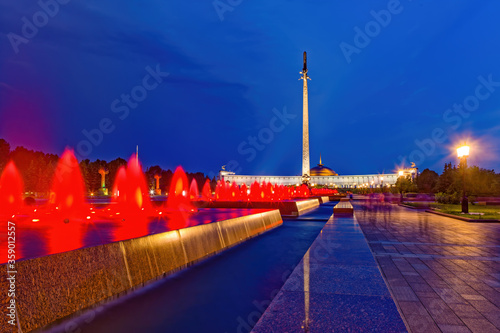 Fountains with red lights in Victory Park Poklonnaya Gora. Night illumination, summer evening in the city. Background - Victory Memorial in World War II.