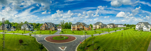 Aerial panorama of new neighborhood street with luxury real estate properties, mansions, brick covered villas with a roundabout and blue sky in Maryland USA